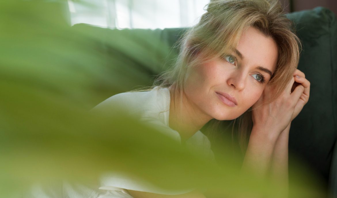 Femme songeuse sur son canapé avec une plante qui est au premier-plan
