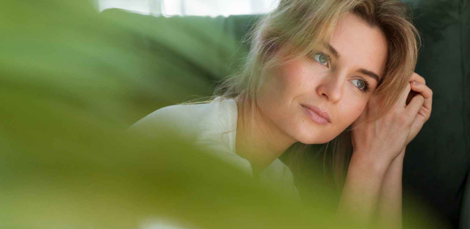 Femme songeuse sur son canapé avec une plante qui est au premier-plan