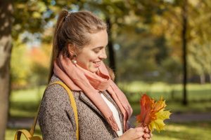 Femme avec écharpe et manteau qui sourit en tenant des feuilles d'arbre